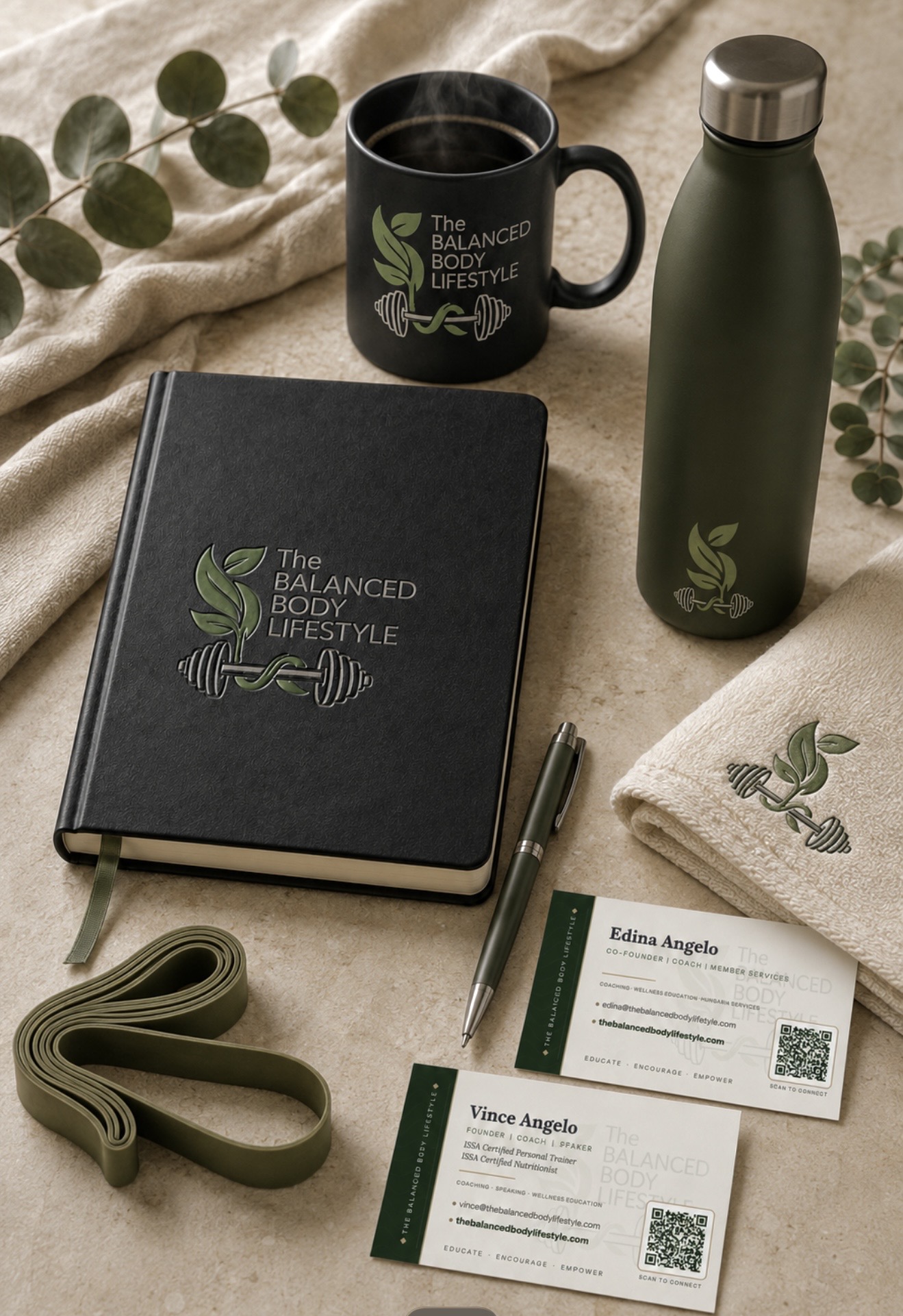 The Balanced Body Lifestyle signature collection: a closed wellness journal, branded mug, water bottle, folded towel, resistance band, pen, and business cards