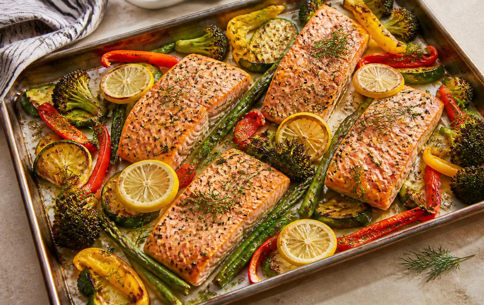 Sheet pan of lemon herb salmon fillets with roasted broccoli, zucchini, asparagus, bell peppers and lemon slices